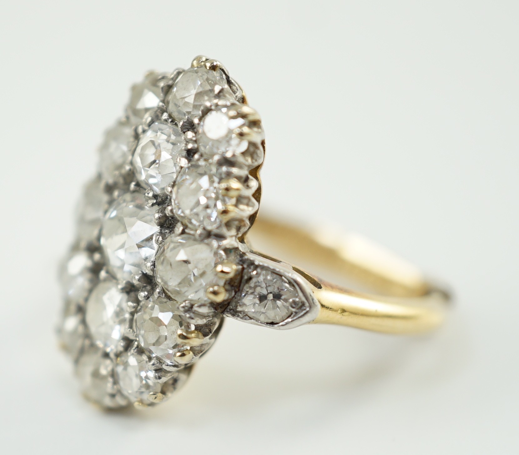 An 18ct gold and oval diamond cluster dress ring, with diamond set shoulders